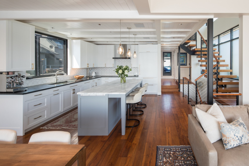 Photo of a transitional l-shaped open plan kitchen in Seattle with an undermount sink, shaker cabinets, white cabinets, white splashback, panelled appliances, medium hardwood floors, with island, brown floor, black benchtop and timber.