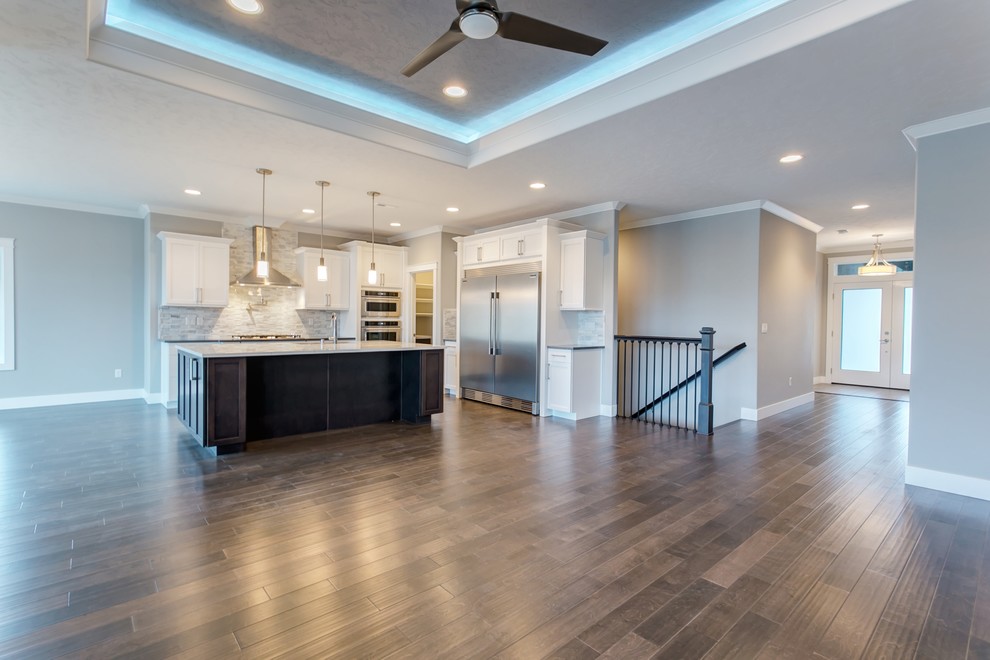 Open concept kitchen - mid-sized transitional l-shaped medium tone wood floor open concept kitchen idea in Seattle with an undermount sink, shaker cabinets, white cabinets, quartz countertops, gray backsplash, stone tile backsplash, stainless steel appliances and an island