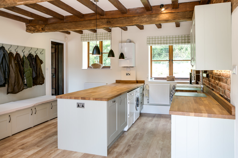 Country laundry room in Gloucestershire with an undermount sink, recessed-panel cabinets, white cabinets, wood benchtops, white walls, light hardwood floors, a side-by-side washer and dryer and brown benchtop.