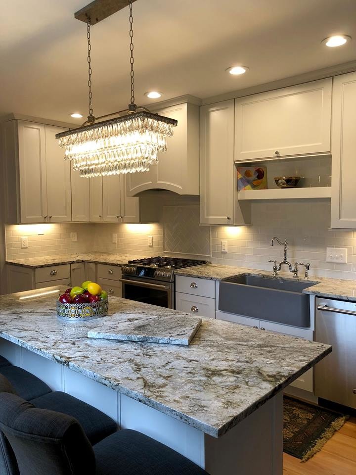 Example of a large transitional l-shaped light wood floor and beige floor eat-in kitchen design in Raleigh with a farmhouse sink, white cabinets, granite countertops, stainless steel appliances, an island, recessed-panel cabinets, white backsplash, subway tile backsplash and gray countertops