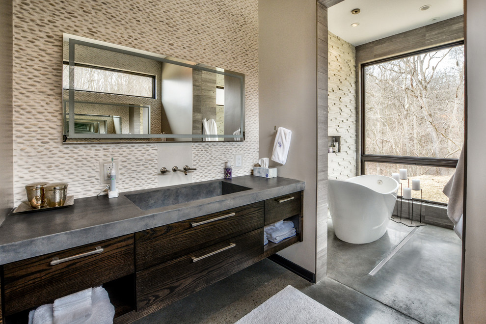 Design ideas for a contemporary master bathroom in Other with flat-panel cabinets, dark wood cabinets, a freestanding tub, concrete floors, an integrated sink, concrete benchtops, grey floor, beige tile, pebble tile and beige walls.