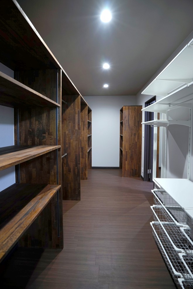 Mid-sized modern gender-neutral walk-in wardrobe in Other with open cabinets, brown cabinets, plywood floors, brown floor and wallpaper.