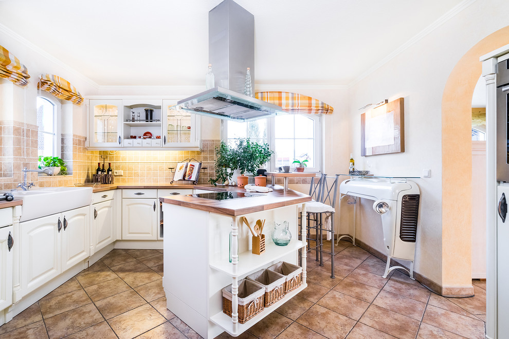 This is an example of a mid-sized mediterranean u-shaped separate kitchen in Other with a farmhouse sink, beaded inset cabinets, white cabinets, wood benchtops, beige splashback, porcelain splashback, no island and ceramic floors.