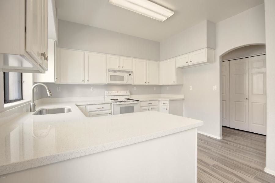 Example of a transitional u-shaped porcelain tile and gray floor eat-in kitchen design in Phoenix with an undermount sink, shaker cabinets, white cabinets, quartz countertops, white backsplash, quartz backsplash, stainless steel appliances, no island and white countertops