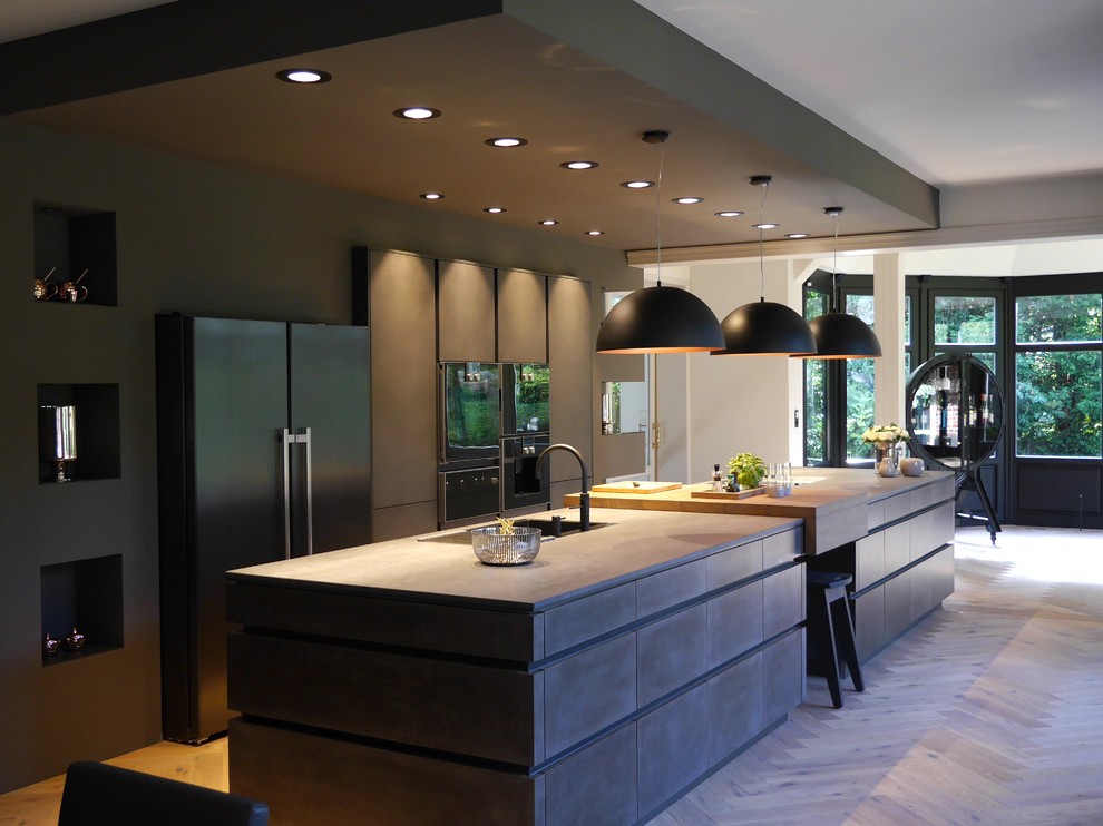 Design ideas for an expansive contemporary galley eat-in kitchen in Bremen with a drop-in sink, flat-panel cabinets, black cabinets, solid surface benchtops, black appliances, medium hardwood floors, with island, brown floor and black benchtop.