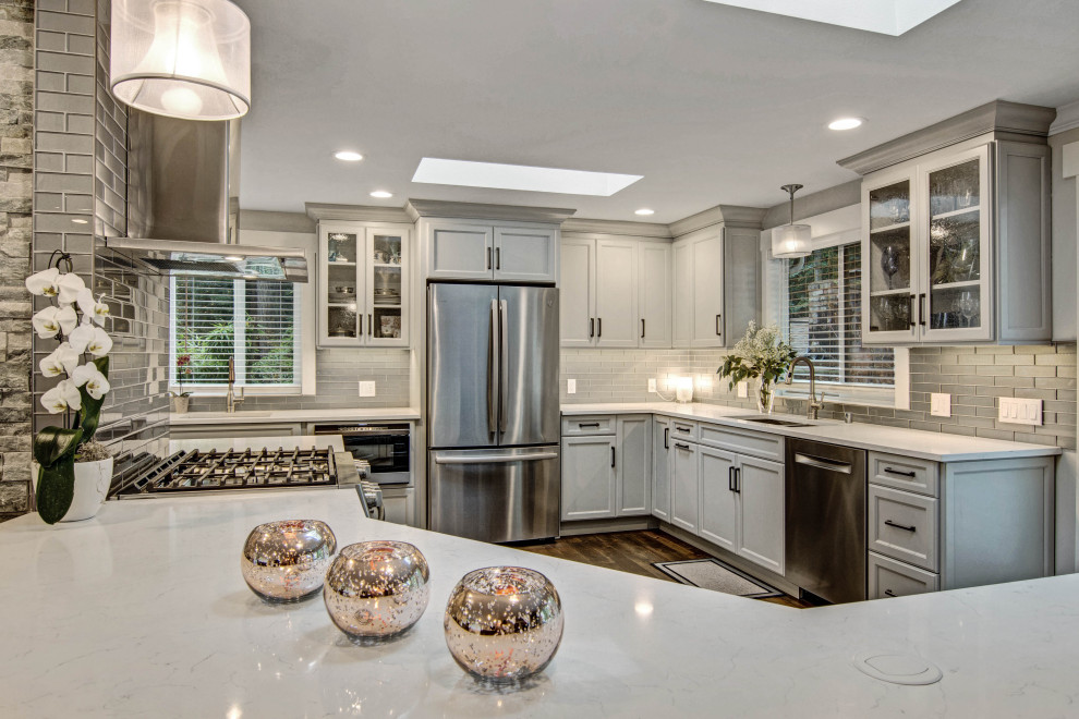 Example of a transitional medium tone wood floor and brown floor open concept kitchen design in Seattle with an undermount sink, recessed-panel cabinets, gray cabinets, quartz countertops, gray backsplash, subway tile backsplash, stainless steel appliances, a peninsula and white countertops