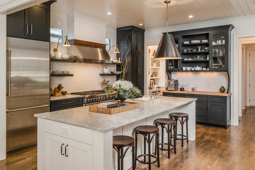 Country l-shaped kitchen in Nashville with a farmhouse sink, recessed-panel cabinets, black cabinets, white splashback, subway tile splashback, stainless steel appliances, dark hardwood floors, with island and brown floor.