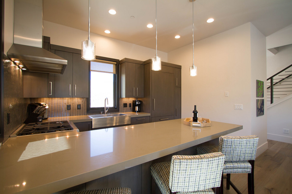 Small transitional l-shaped eat-in kitchen in Salt Lake City with a farmhouse sink, flat-panel cabinets, dark wood cabinets, solid surface benchtops, brown splashback, mosaic tile splashback, stainless steel appliances, light hardwood floors, a peninsula and beige floor.