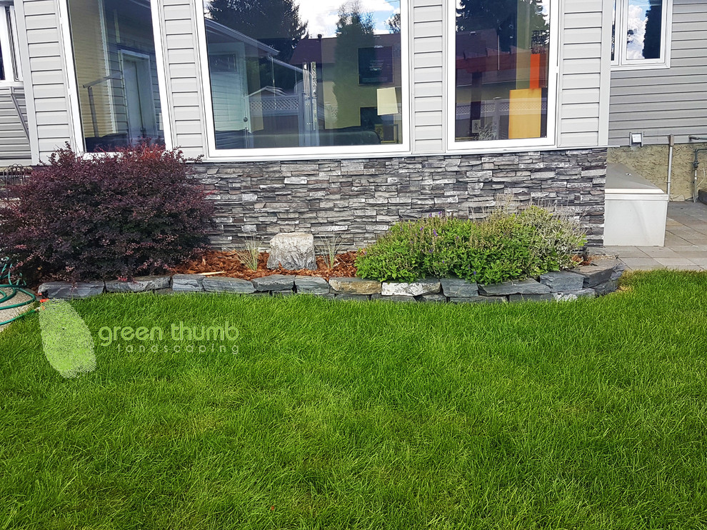 This is an example of a rustic full sun backyard stone retaining wall landscape in Edmonton for summer.