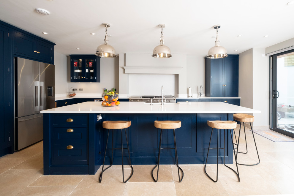 This is an example of a transitional l-shaped kitchen in Cardiff with a farmhouse sink, shaker cabinets, blue cabinets, stainless steel appliances, with island, beige floor and white benchtop.