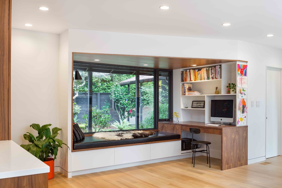 This is an example of a small midcentury home office in Portland with white walls, light hardwood floors, no fireplace, a built-in desk and beige floor.