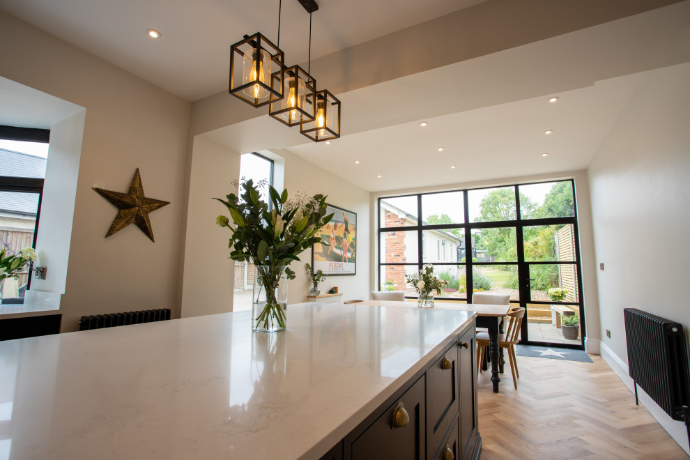 Inspiration for a medium sized classic cream and black kitchen/diner in Essex with shaker cabinets, black cabinets, quartz worktops, white splashback, medium hardwood flooring, an island, brown floors, white worktops and a feature wall.