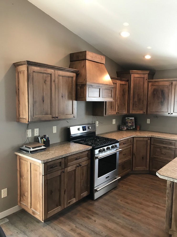 Example of a large mountain style l-shaped medium tone wood floor and brown floor open concept kitchen design with an undermount sink, recessed-panel cabinets, medium tone wood cabinets, stainless steel appliances, an island and laminate countertops