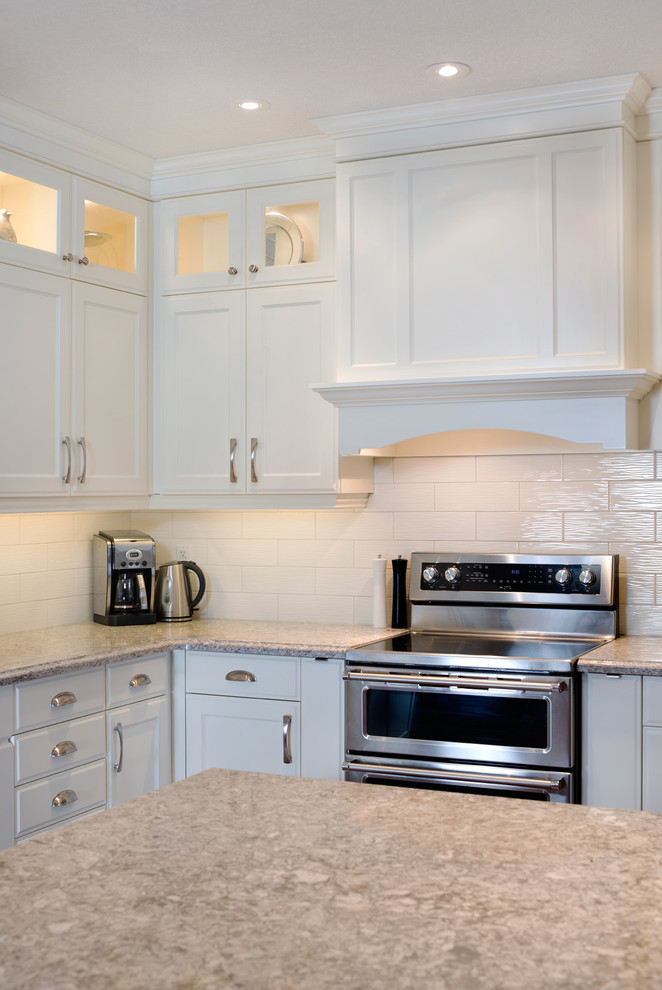 Inspiration for a large transitional l-shaped medium tone wood floor kitchen remodel in Toronto with an undermount sink, recessed-panel cabinets, white cabinets, quartz countertops, white backsplash, subway tile backsplash, stainless steel appliances and an island