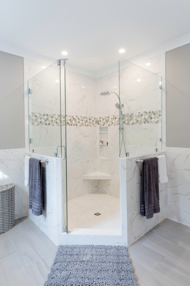 Cette photo montre une grande salle de bain principale chic en bois clair avec un placard avec porte à panneau surélevé, une douche d'angle, un carrelage blanc, des carreaux de porcelaine, un mur gris, un sol en carrelage de porcelaine, un lavabo encastré, un plan de toilette en quartz modifié, un sol gris, une cabine de douche à porte battante, un plan de toilette beige, une niche, meuble double vasque et meuble-lavabo encastré.