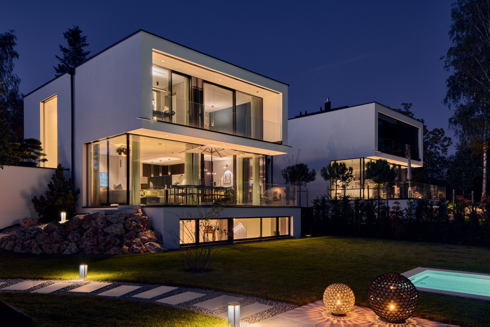 Contemporary two-storey stucco white duplex exterior in Munich with a hip roof, a metal roof and a black roof.