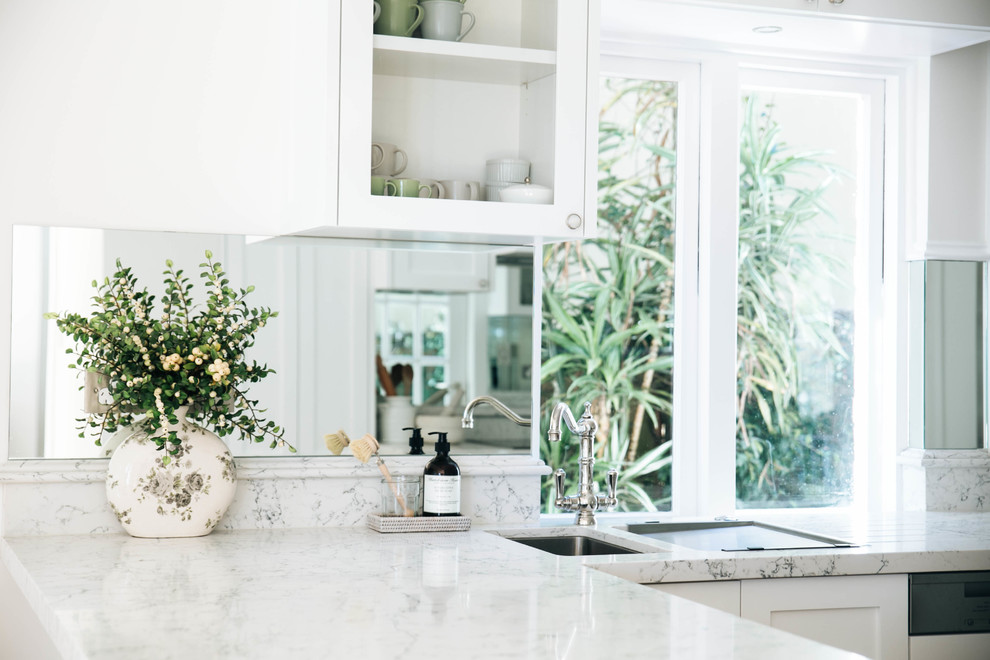 Mid-sized traditional l-shaped eat-in kitchen in Sydney with an undermount sink, recessed-panel cabinets, white cabinets, quartz benchtops, black appliances, medium hardwood floors, white benchtop and mirror splashback.