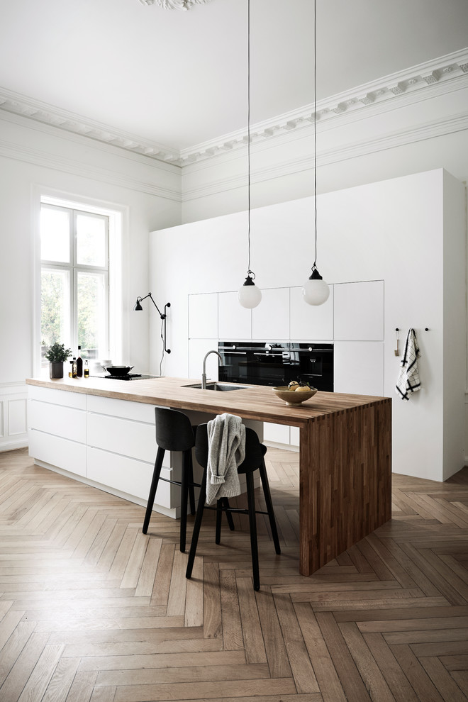 Scandinavian galley kitchen in Copenhagen with an undermount sink, flat-panel cabinets, wood benchtops, black appliances, medium hardwood floors, with island and brown floor.