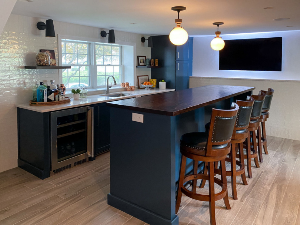 Photo of a transitional wet bar in Boston with an undermount sink, flat-panel cabinets, blue cabinets, wood benchtops, white splashback, ceramic splashback, porcelain floors, brown floor and brown benchtop.