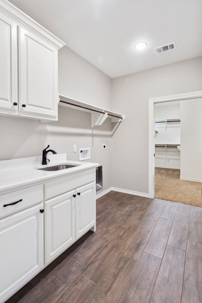 This is an example of a traditional utility room in Austin with an integrated sink, beaded inset cabinets, white cabinets, quartz benchtops, medium hardwood floors, a side-by-side washer and dryer, brown floor and multi-coloured benchtop.