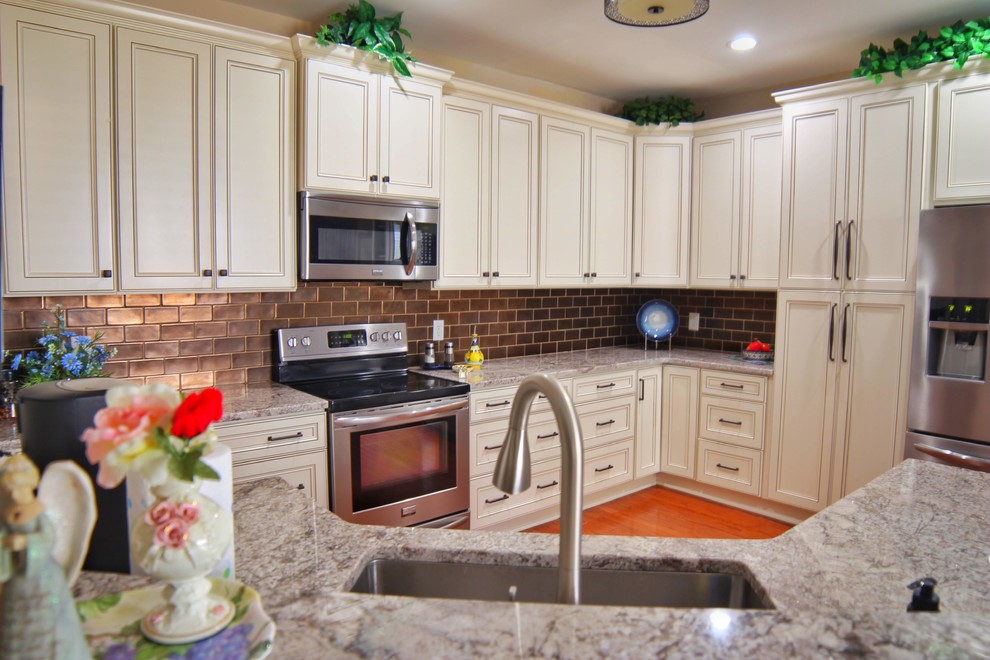 Inspiration for a mid-sized u-shaped medium tone wood floor and brown floor kitchen remodel in Charleston with an undermount sink, raised-panel cabinets, beige cabinets, granite countertops, brown backsplash, ceramic backsplash, stainless steel appliances and beige countertops