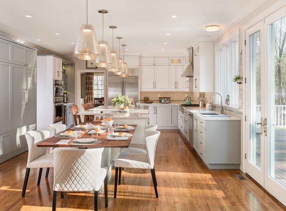 This is an example of a transitional u-shaped eat-in kitchen in Boston with an undermount sink, shaker cabinets, grey cabinets, beige splashback, mosaic tile splashback, stainless steel appliances, medium hardwood floors, with island, brown floor and white benchtop.