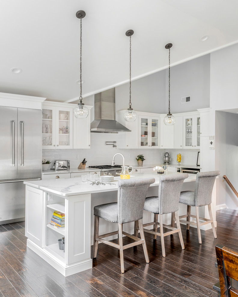 Design ideas for a large transitional l-shaped kitchen in Boston with recessed-panel cabinets, white splashback, with island, a farmhouse sink, white cabinets, stainless steel appliances, dark hardwood floors and brown floor.