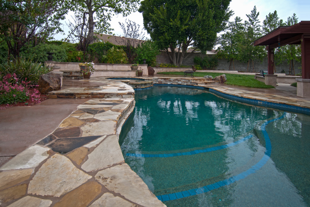 Inspiration for a large eclectic backyard custom-shaped natural pool in Los Angeles with a hot tub and natural stone pavers.
