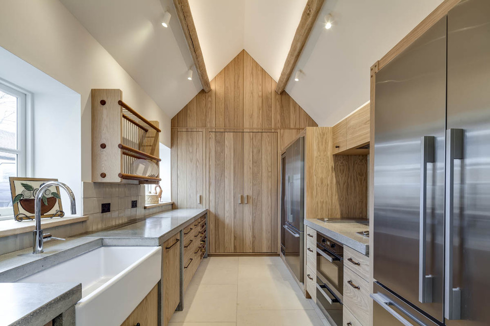 Country galley kitchen in Gloucestershire with a farmhouse sink, flat-panel cabinets, light wood cabinets, concrete benchtops, stainless steel appliances, limestone floors, no island and beige floor.