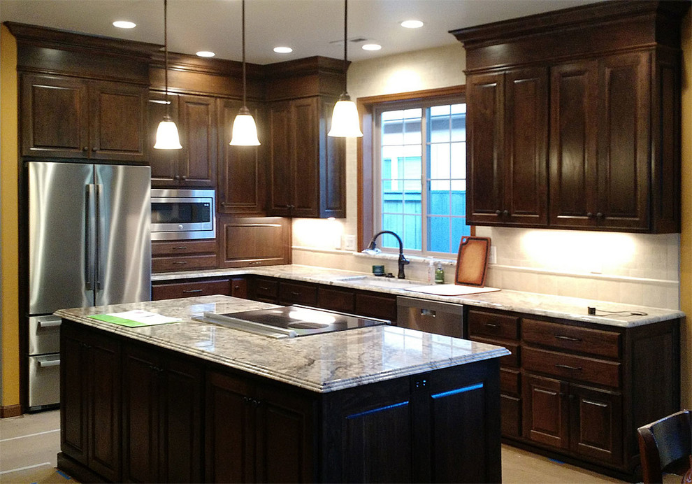 Inspiration for a l-shaped kitchen remodel with an integrated sink, raised-panel cabinets, brown cabinets, stainless steel appliances and an island
