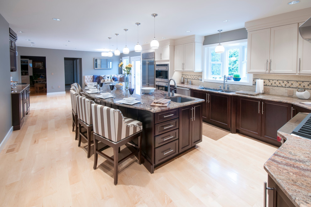 Inspiration for an expansive transitional l-shaped open plan kitchen in Providence with with island, shaker cabinets, white cabinets, granite benchtops, beige splashback, stone tile splashback, stainless steel appliances, an undermount sink and light hardwood floors.
