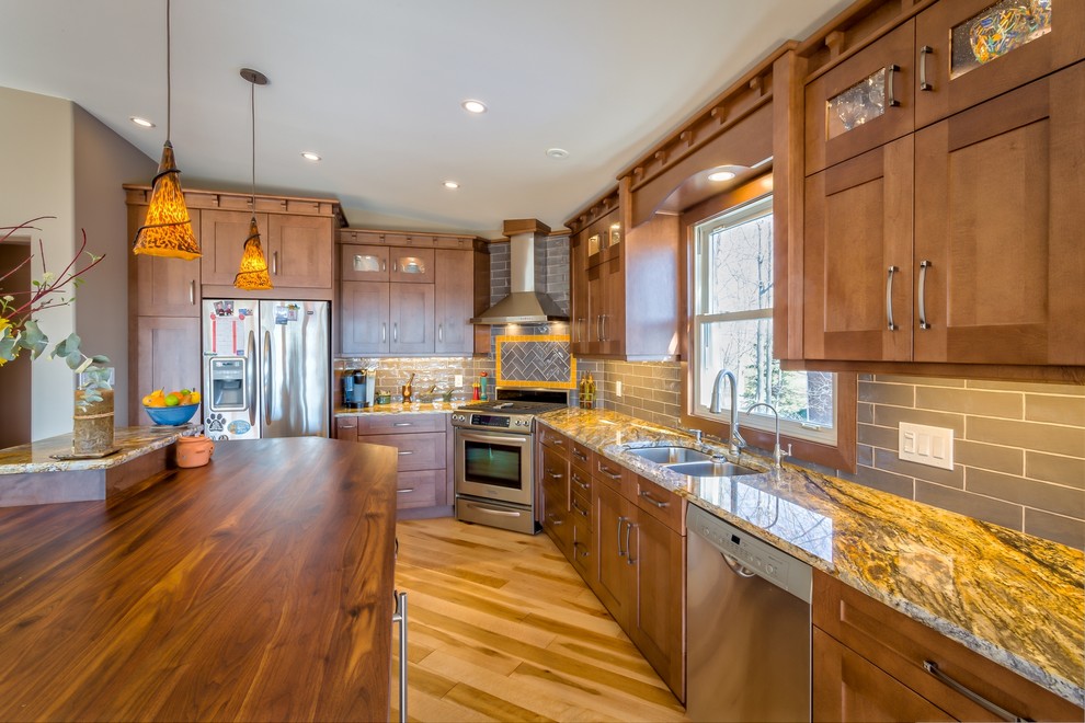 This is an example of a mid-sized arts and crafts l-shaped open plan kitchen in Ottawa with a double-bowl sink, shaker cabinets, brown cabinets, granite benchtops, grey splashback, subway tile splashback, stainless steel appliances, light hardwood floors and with island.