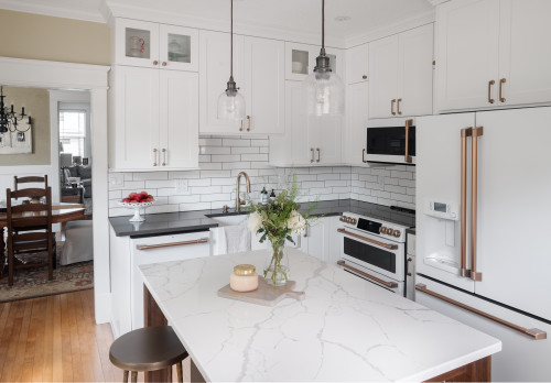 Bright modern kitchen with white shaker kitchen cabinets, black countertops, subway tile backsplash and a marble island with brass accents.