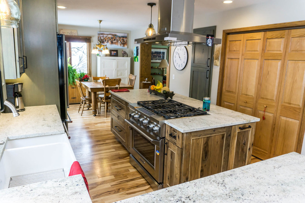 Example of a large mountain style light wood floor and brown floor open concept kitchen design with beaded inset cabinets, distressed cabinets, granite countertops, an island and white countertops