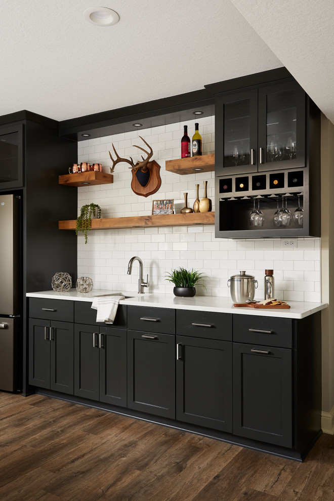 Photo of a mid-sized transitional single-wall wet bar in Minneapolis with an undermount sink, shaker cabinets, black cabinets, quartzite benchtops, white splashback, subway tile splashback, vinyl floors, brown floor and white benchtop.