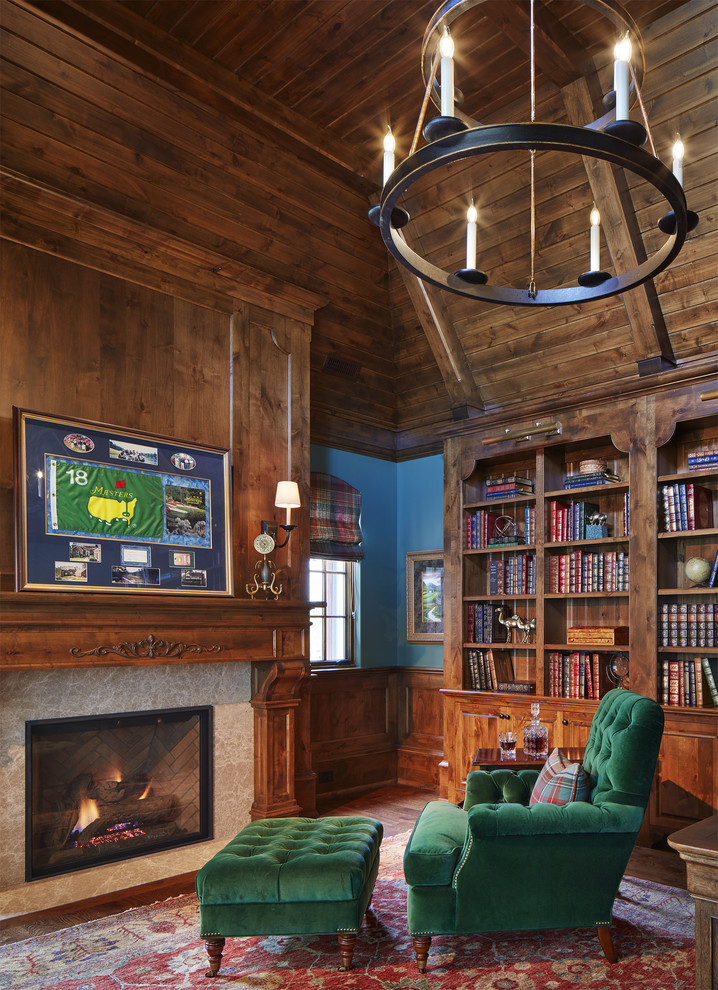 Inspiration for a large traditional home office in Minneapolis with a library, brown walls, dark hardwood floors, a standard fireplace, a wood fireplace surround and brown floor.