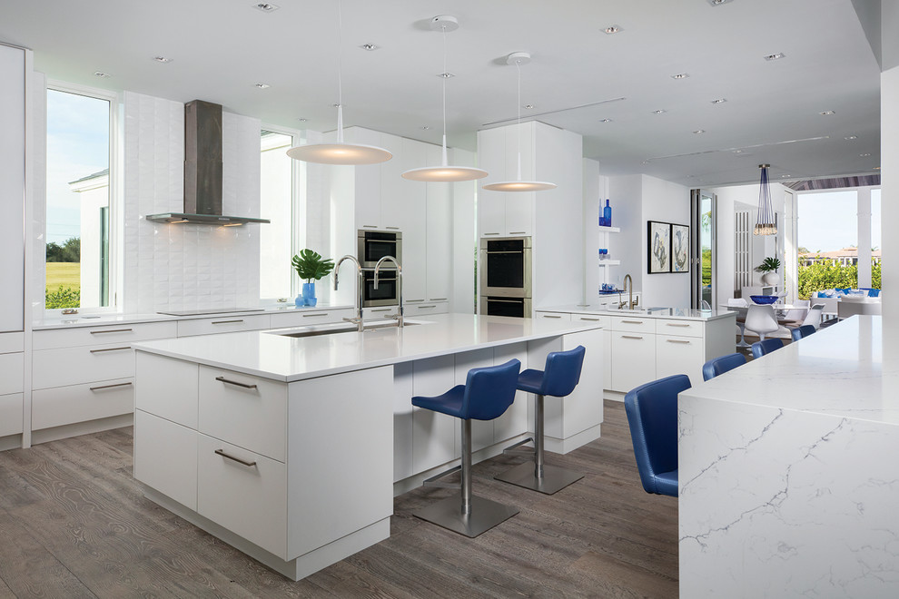 Photo of a large contemporary l-shaped kitchen in Other with flat-panel cabinets, white cabinets, white splashback, multiple islands, an undermount sink, stainless steel appliances, dark hardwood floors and brown floor.