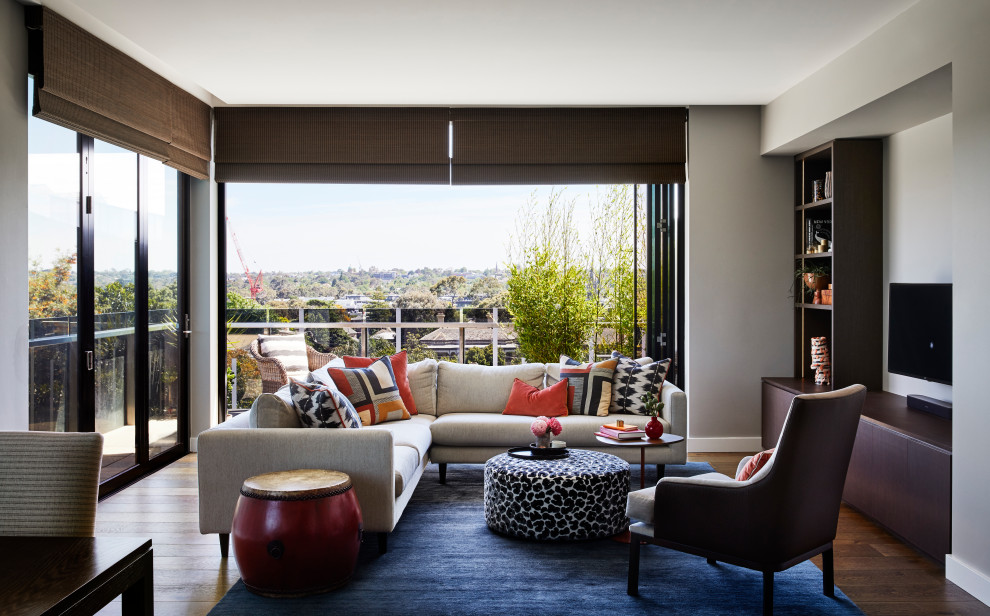 Mittelgroßes, Offenes Modernes Wohnzimmer mit grauer Wandfarbe, braunem Holzboden, TV-Wand und braunem Boden in Melbourne