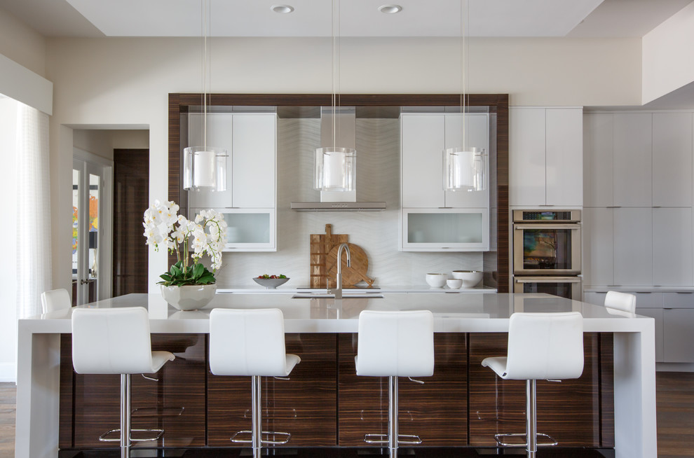 Photo of a contemporary kitchen in Jacksonville with an undermount sink, flat-panel cabinets, white cabinets, white splashback, stainless steel appliances, dark hardwood floors, with island and white benchtop.