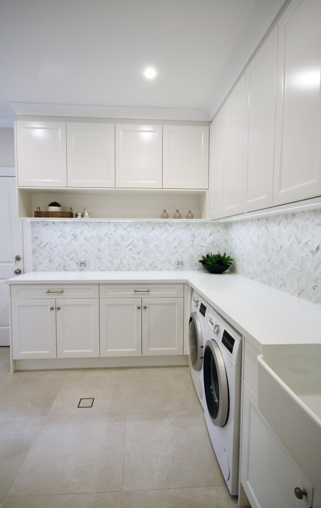 Inredning av ett stort vit l-format vitt grovkök, med en rustik diskho, luckor med infälld panel, vita skåp, bänkskiva i kvarts, grått stänkskydd, stänkskydd i marmor, grå väggar, klinkergolv i keramik, en tvättmaskin och torktumlare bredvid varandra och grått golv