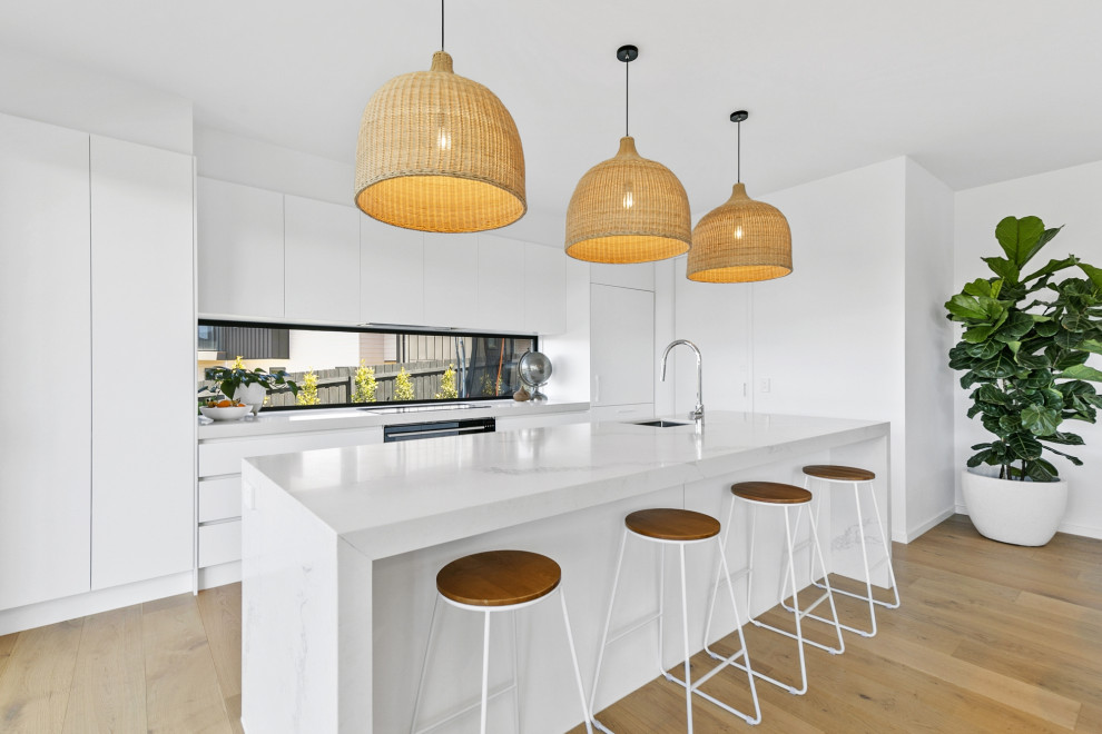 Inspiration for a large contemporary galley open plan kitchen in Geelong with an undermount sink, flat-panel cabinets, white cabinets, solid surface benchtops, window splashback, stainless steel appliances, light hardwood floors, with island and white benchtop.