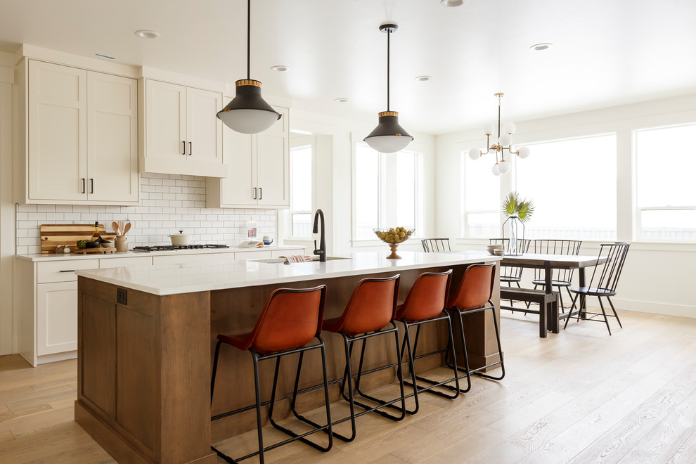 Inspiration for a transitional galley eat-in kitchen in Boise with an undermount sink, shaker cabinets, white cabinets, white splashback, subway tile splashback, light hardwood floors, with island, beige floor and white benchtop.