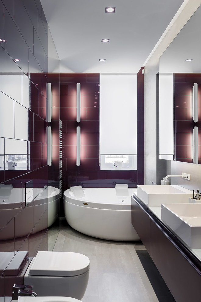 На фото: главная ванная комната среднего размера с угловой ванной, инсталляцией, серой плиткой, керамогранитной плиткой, фиолетовыми стенами, полом из керамогранита, настольной раковиной и стеклянной столешницей