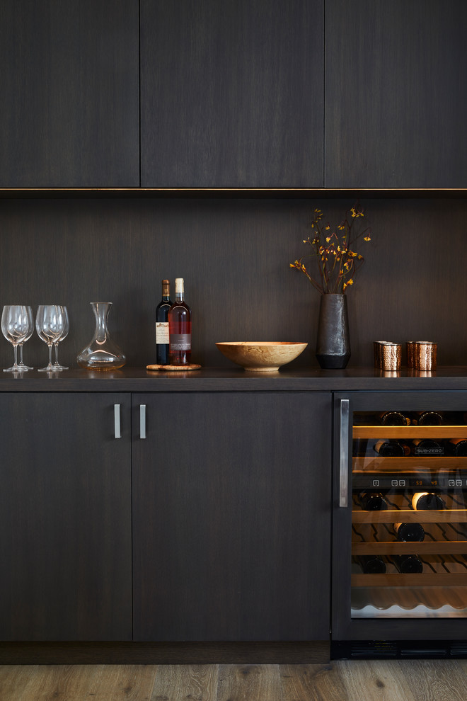 Photo of a contemporary home bar in San Francisco with flat-panel cabinets, dark wood cabinets, brown splashback, medium hardwood floors and brown floor.