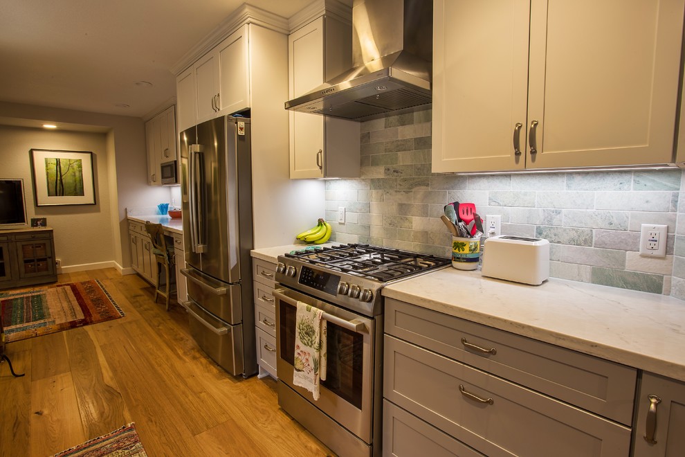 Open concept kitchen - large transitional galley light wood floor and brown floor open concept kitchen idea in Sacramento with a farmhouse sink, shaker cabinets, gray cabinets, quartz countertops, gray backsplash, stone tile backsplash, stainless steel appliances, no island and white countertops