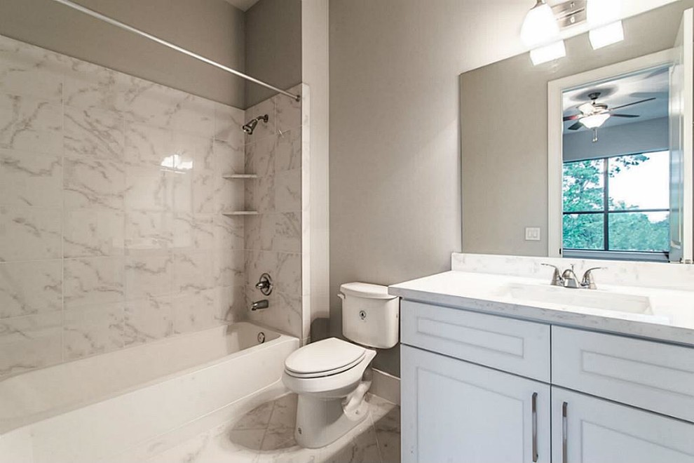 Design ideas for a small transitional 3/4 bathroom in Houston with shaker cabinets, white cabinets, an alcove tub, a shower/bathtub combo, a one-piece toilet, white tile, stone tile, grey walls, marble floors, an undermount sink and engineered quartz benchtops.