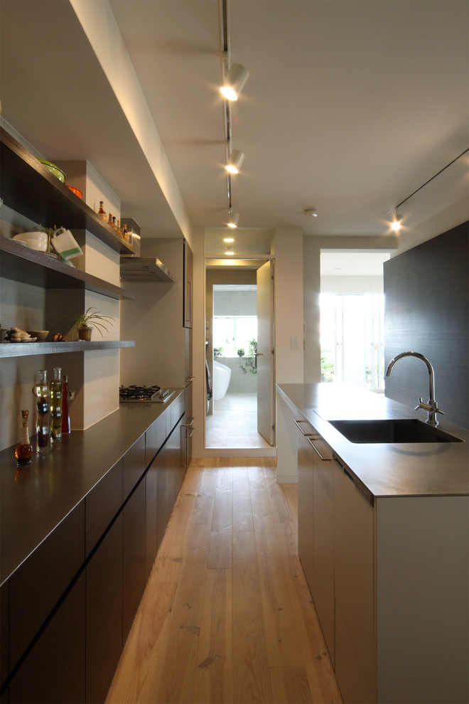 Inspiration for a mid-sized asian galley kitchen in Osaka with an integrated sink, stainless steel benchtops, with island, flat-panel cabinets, dark wood cabinets, black splashback, medium hardwood floors, brown floor and brown benchtop.