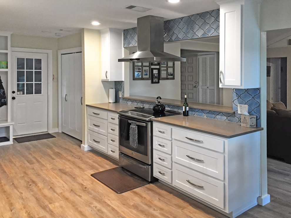 Mid-sized transitional galley vinyl floor and brown floor kitchen pantry photo with an undermount sink, shaker cabinets, white cabinets, solid surface countertops, blue backsplash, ceramic backsplash, stainless steel appliances and no island