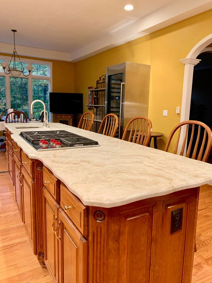 This is an example of a large arts and crafts l-shaped eat-in kitchen in Indianapolis with an undermount sink, raised-panel cabinets, medium wood cabinets, quartzite benchtops, white splashback, ceramic splashback, stainless steel appliances, medium hardwood floors, with island, brown floor and white benchtop.