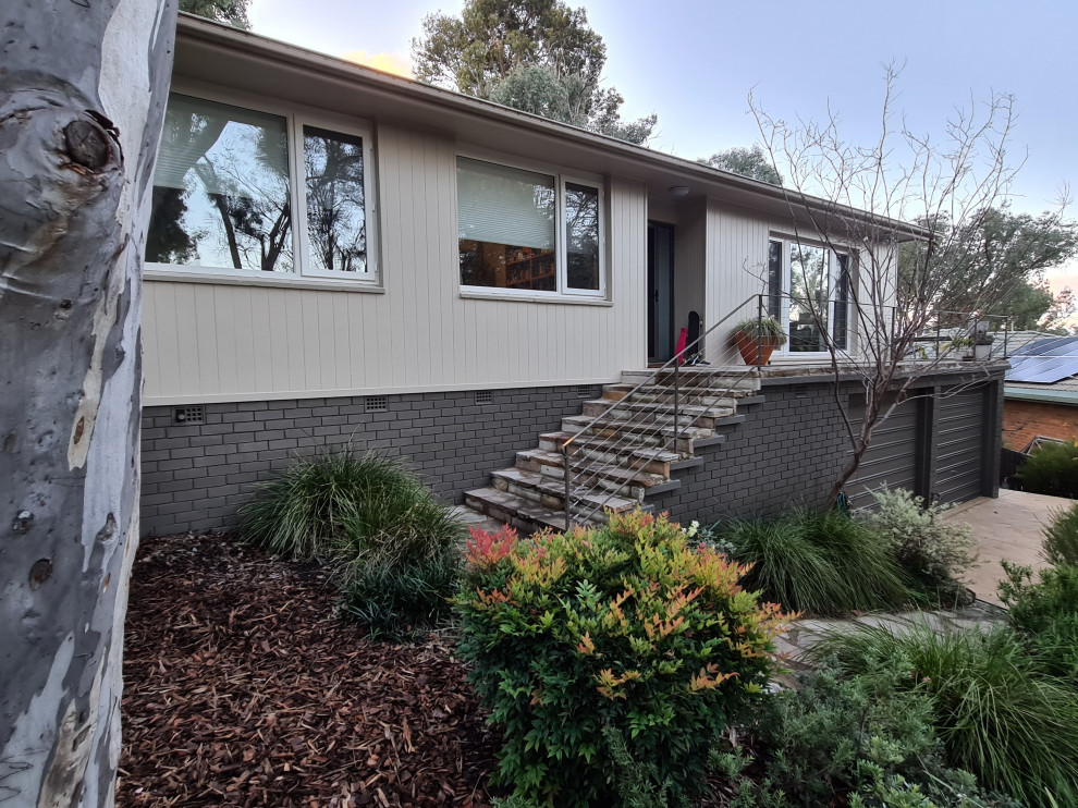 This is an example of a mid-sized midcentury one-storey beige house exterior in Canberra - Queanbeyan with concrete fiberboard siding and a tile roof.